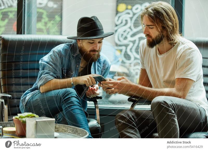 Männer sitzen und telefonieren in einem Cafe Café Zeigen Finger Smartphone Freundschaft Lächeln sprechend genießend Erwachsener gutaussehend Lifestyle