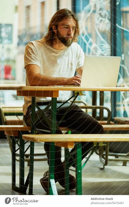Hübscher Mann sitzt am Tisch und tippt auf einem Laptop gutaussehend Schnurrbart arbeiten Erwachsener Lifestyle Bartstoppel Frisur Fröhlichkeit bärtig Model