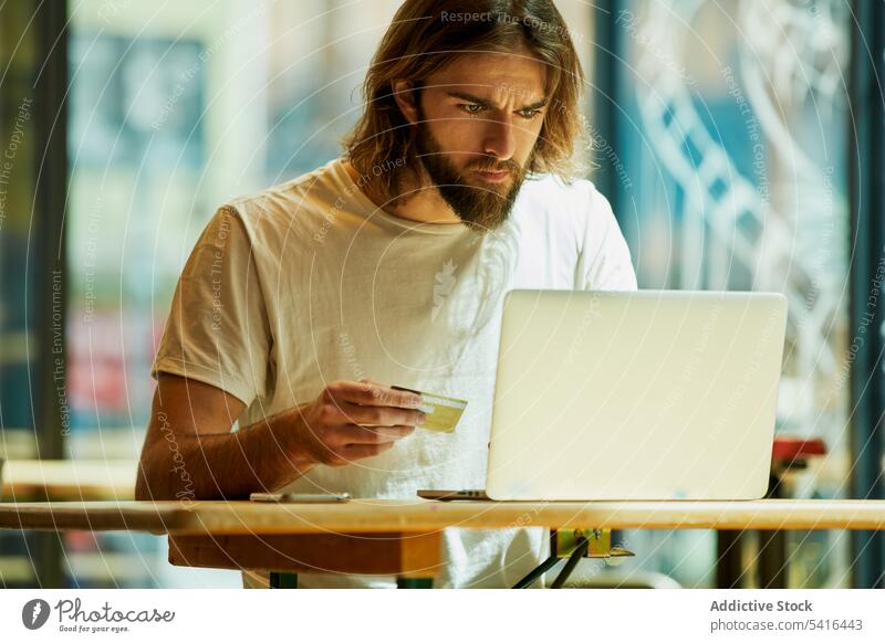 Hübscher Mann sitzt am Tisch und tippt auf einem Laptop Elektronischer Geschäftsverkehr kaufen Kredit Postkarte jung online gutaussehend Erwachsener Zahlung