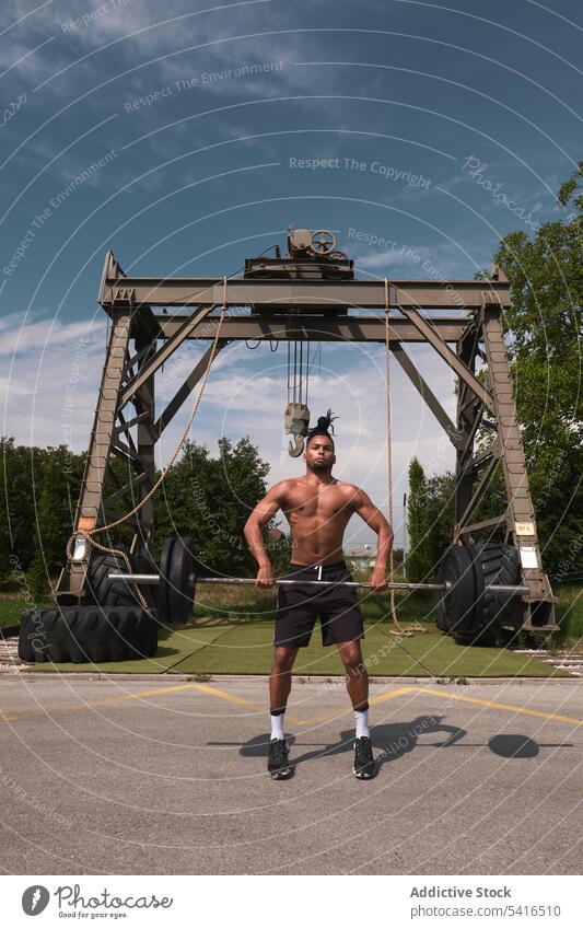 Schwarzer Mann mit Langhantel im Fitnessstudio im Freien Curl-Hantel Heben Übung Training ohne Hemd Afroamerikaner Wolken Himmel männlich Gewicht passen Stärke