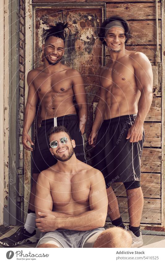 Muskulöse multiethnische Männer in der Nähe eines schäbigen Gebäudes muskulös selbstbewusst Fitnessstudio rassenübergreifend jung ohne Hemd stark hispanisch