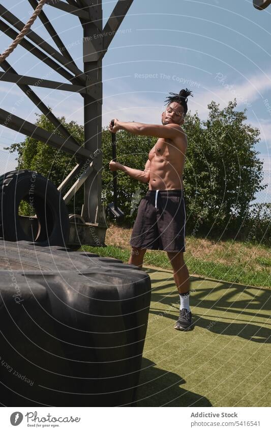 Muskulöser schwarzer Mann hämmert Reifen in einem Fitnessstudio im Freien Hammer Übung schlagend ohne Hemd muskulös anstrengen Training Athlet männlich Sport