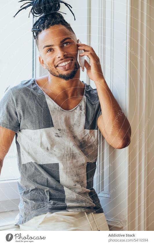 Ethnisch geflochtener Mann mit Smartphone ethnisch Frisur Zöpfe kreativ Fenster jung männlich Afroamerikaner Person gutaussehend attraktiv Sprechen nachdenklich