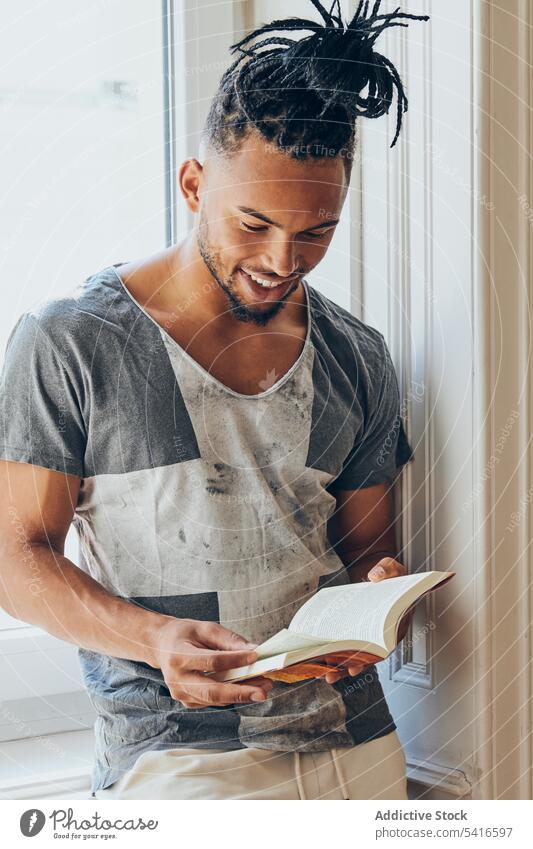 Ethnischer Mann steht am Fenster und liest ethnisch Frisur Geflecht Zöpfe kreativ lesen Buch jung männlich Afroamerikaner Person gutaussehend attraktiv