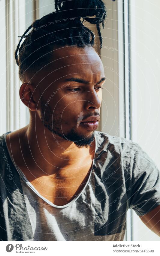Nachdenklicher ethnischer Mann auf der Fensterbank sitzend Frisur cornrows geflochten jung nachdenklich männlich Afroamerikaner schwarz Person gutaussehend