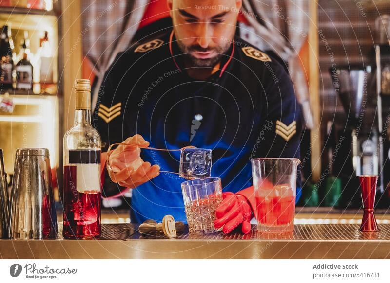 Barkeeper in roten Handschuhen hält großen Eiswürfel i Alkohol Nachtclub Mischen mitreißend vorbereitend Barmann Cocktail Uniform Glas trinken Getränk
