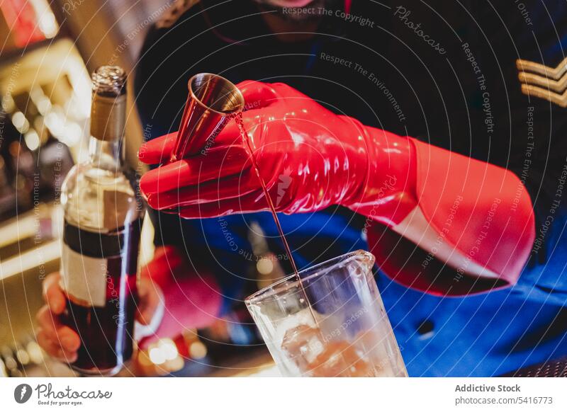 Barkeeper mit roten Handschuhen gießt ein Getränk in eine Flasche Mischen Alkohol Gießen Nachtclub mitreißend vorbereitend Barmann Cocktail Uniform Eiswürfel