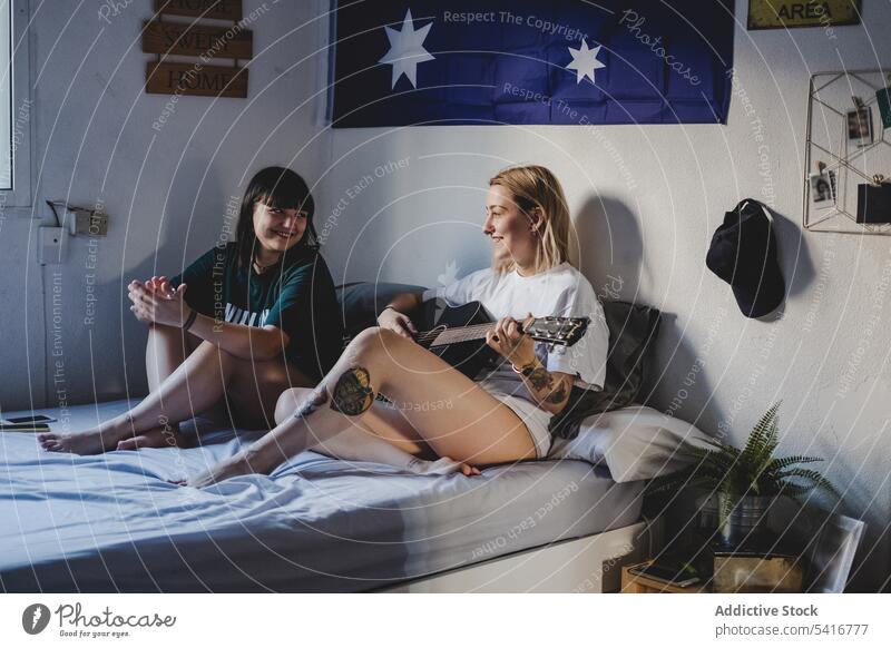 Lesbisches Paar spielt Gitarre auf dem Bett lesbisch Spielen heimwärts Sitzen heiter die sich gegenseitig ansehen jung Partnerschaft Frauen lgbt romantisch