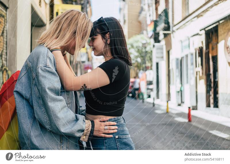 Lesbisches Paar mit LGBT-Flagge auf der Straße stehend lesbisch Fahne lgbt umarmend Glück Großstadt jung Zusammensein Frauen lässig Homosexualität Stolz