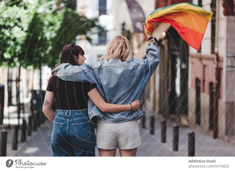 Lesbisches Paar mit LGBT-Flagge auf der Straße lesbisch Fahne lgbt laufen umarmend Glück winkend Großstadt jung Zusammensein Frauen lässig Homosexualität Stolz