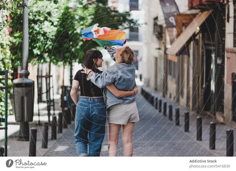 Lesbisches Paar mit LGBT-Flagge auf der Straße lesbisch Fahne lgbt laufen umarmend Glück winkend Großstadt jung Zusammensein Frauen lässig Homosexualität Stolz