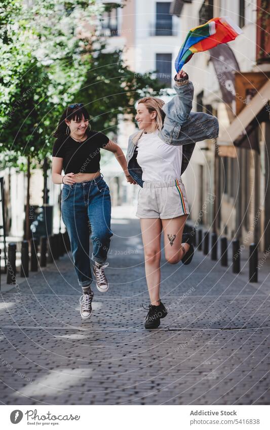 Lesbisches Paar mit LGBT-Flagge auf der Straße lesbisch Fahne lgbt laufen Glück winkend Großstadt jung Zusammensein Frauen lässig Homosexualität Stolz