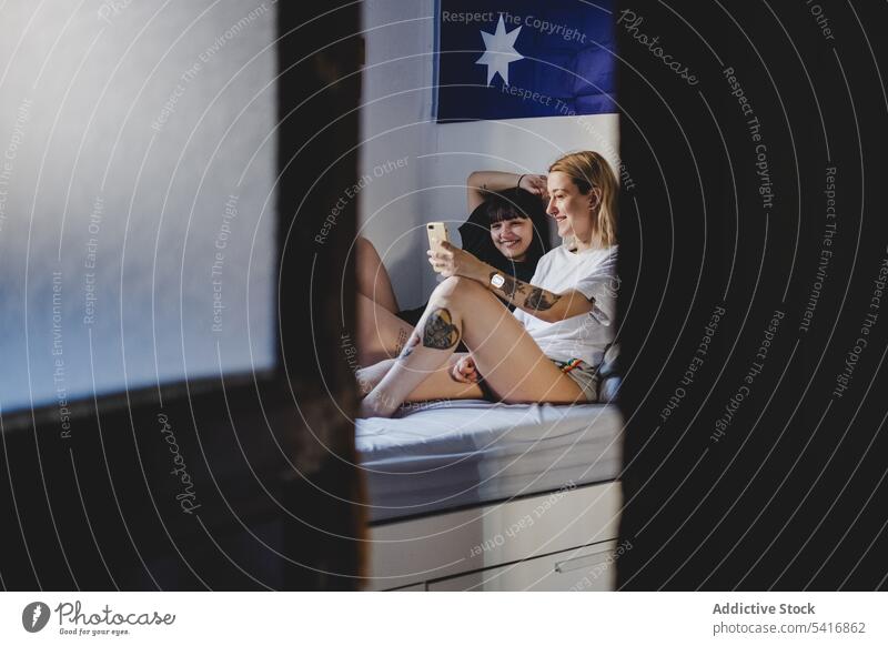 Glückliches lesbisches Paar benutzt Smartphone auf dem Bett Handy benutzend Lächeln Zusammensein Liebe jung Partnerschaft romantisch Frauen Freundin