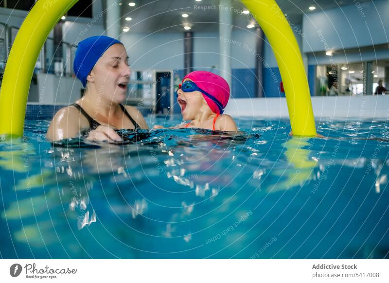 Fröhliches Mädchen schwimmt mit Mutter im Pool Schwimmsport Wasser Park aufgeregt Spaß Wochenende Zusammensein Vergnügen Frau Kind Schutzbrille Hut heiter Glück