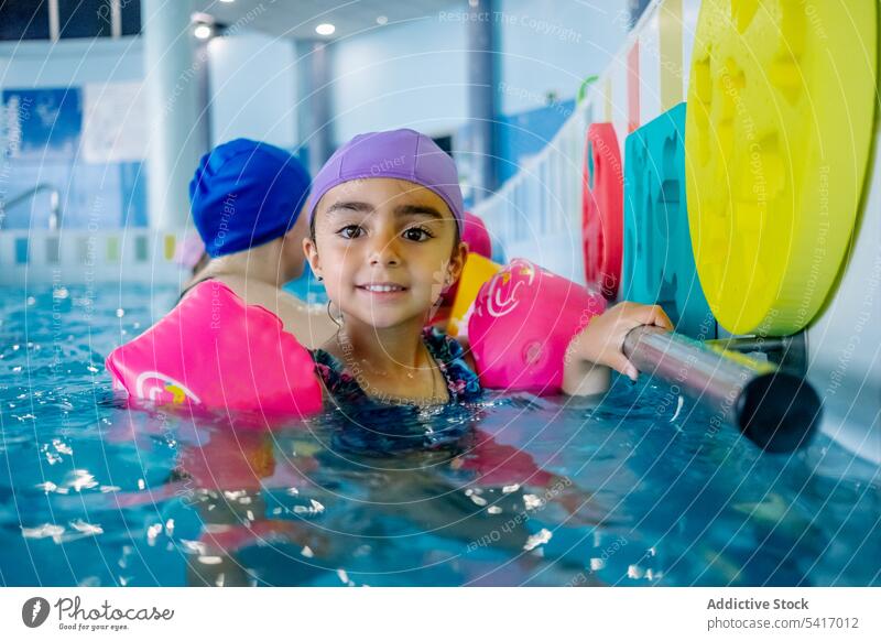 Ethnisches Mädchen mit Schwimmflügeln im Schwimmbad Spielen Wasser Park Schwimmsport Pool aufblasbar Flügel ethnisch Spielzeug Spaß Kind Freude Glück wenig