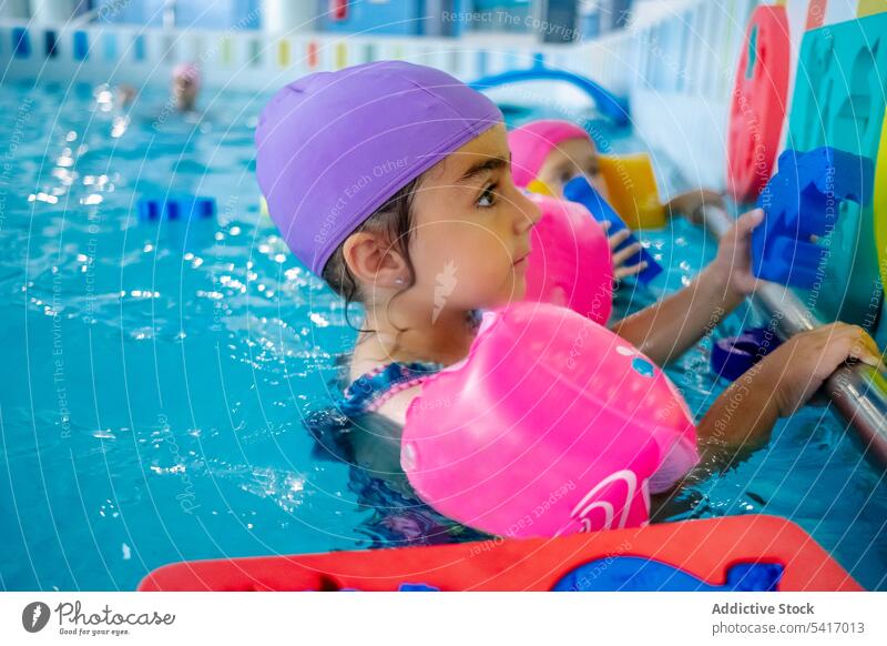 Ethnisches Mädchen mit Schwimmflügeln im Schwimmbad Spielen Wasser Park Schwimmsport Pool aufblasbar Flügel ethnisch Spielzeug Spaß Kind Freude Glück wenig
