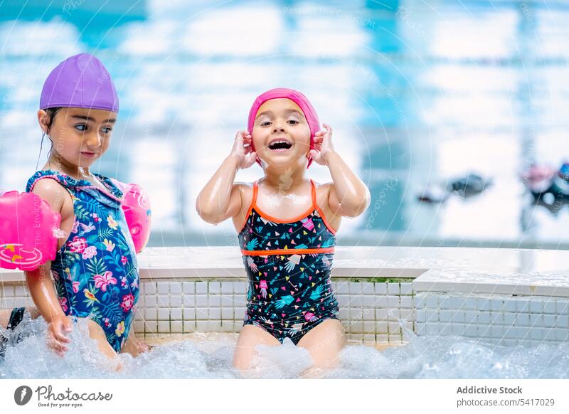 Ethnische Mädchen mit Schwimmflügeln im Schwimmbad Spielen Wasser Park Schwimmsport Pool aufblasbar Flügel ethnisch Spielzeug Spaß Kind Freude Glück wenig