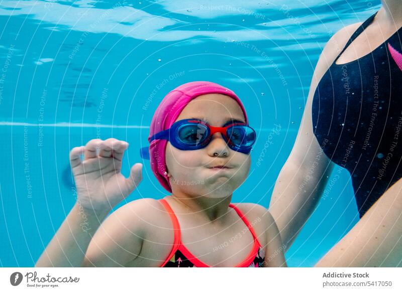 Fröhliches Mädchen beim Unterwasserschwimmen im Pool mit Mutter Schwimmsport Wasser Park aufgeregt Spaß Wochenende Zusammensein Vergnügen Frau Kind Schutzbrille