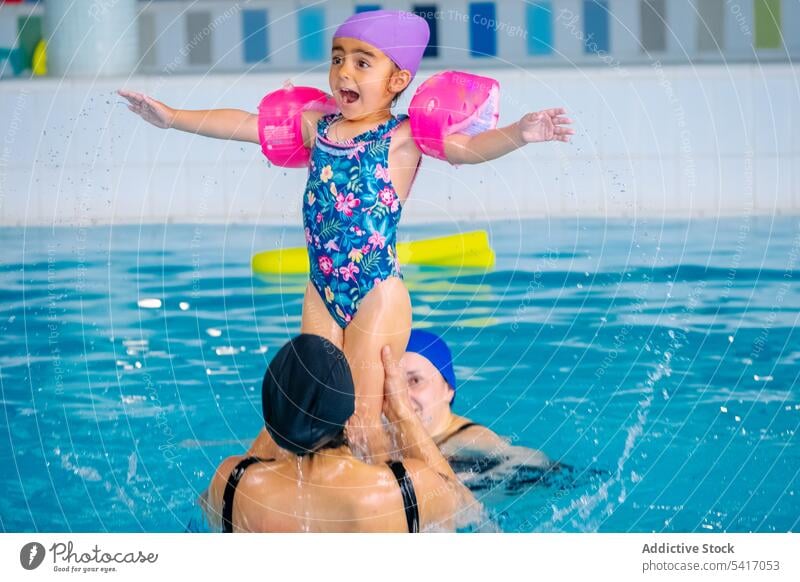 Mutter spielt mit Tochter im Schwimmbad Spaß Wasser Schwimmsport Pool Heben ausgestreckte Arme ethnisch Spielen Zusammensein Familie Eltern Frau Mädchen Kind