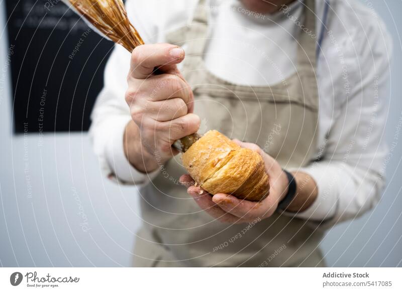 Konditor gießt Schokoladenfüllung in Croissant Mann Füllung Brotbelag Sahne Dessert Küchenchef Kuchen Koch Beruf Arbeit Verrohrung Tasche Gebäck männlich