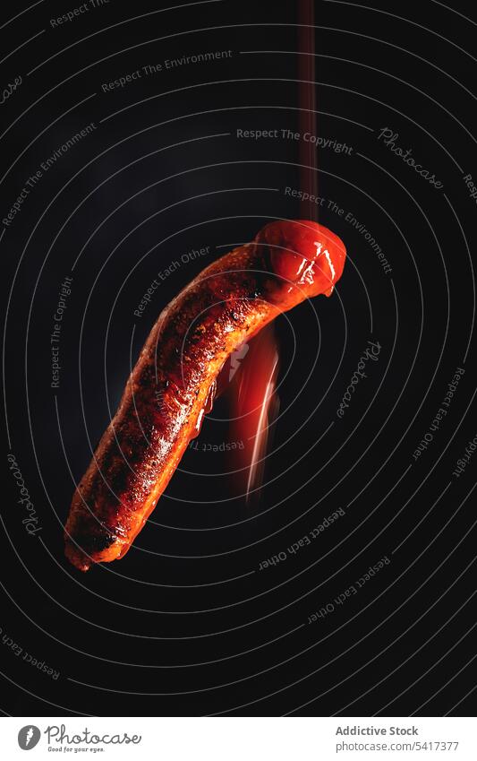 Ketchup fällt auf gegrillte Wurst in einem schwarzen Hintergrund Beschneidungspfad Mahlzeit Gastronomie ungesund Nahaufnahme gebraten Fleisch vorbereitet