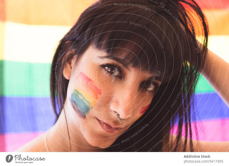 Brünette Frau mit LGBT-Symbol im Gesicht glättet Haare schön lgbt attraktiv jung hübsch sinnlich ernst Freiheit Gleichstellung Rechte heiter Toleranz Regenbogen