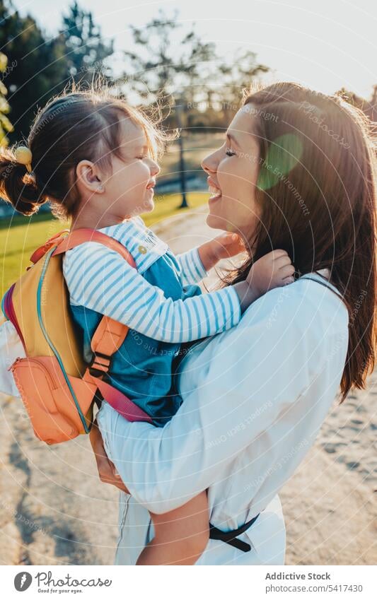 Mutter küsst Tochter im Park sonnig tagsüber umarmend tragen Lifestyle Freizeit Zusammensein Frau Mädchen Kind Rucksack ruhen sich[Akk] entspannen Wochenende