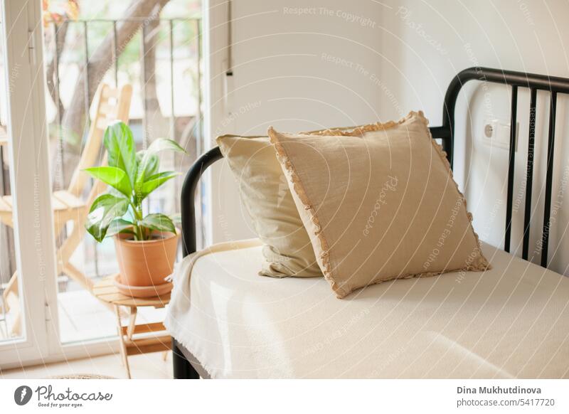 Sofa oder Couch mit beigem Bettzeug und Kissen und grüner Zimmerpflanze bei minimalem Innenausbau. Wachsende Pflanzen und städtischen Dschungel Hobby. Tropische Wohnkultur.