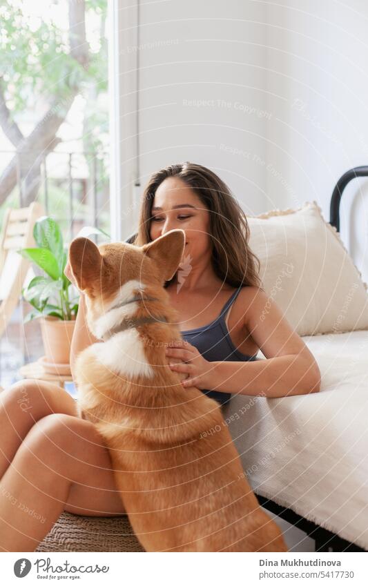 Millennial kaukasische Frau zu Hause mit Corgi Hund. Hundebesitzer und Trainer. Lustige gemütliches Bild der Frau mit Welpe in der Wohnung. Brunette lächelnd mit welsh Corgi Pembroke Hund sitzt auf Couch.