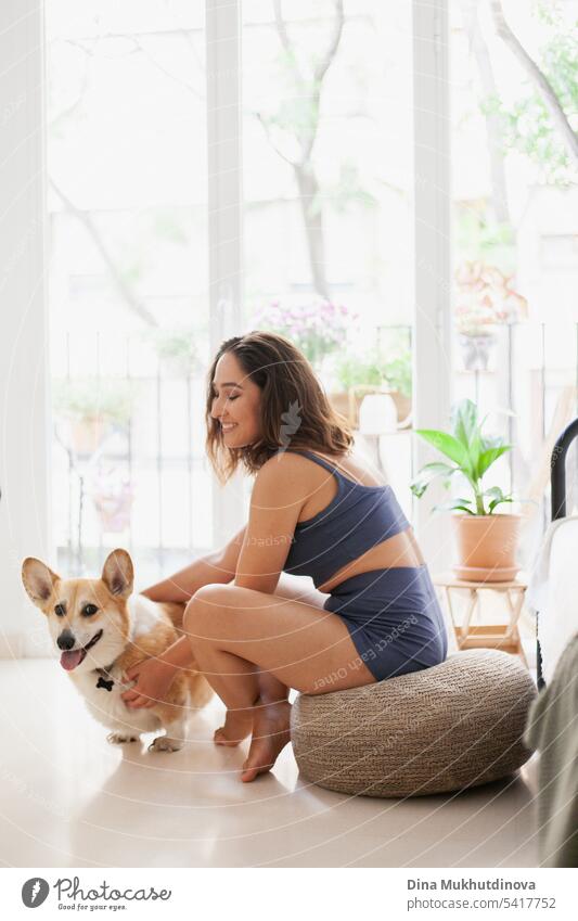 Millennial kaukasische Frau zu Hause mit Corgi Hund. Hundetrainer. Lustige gemütliches Bild der Frau mit Welpe in der Wohnung. Brunette lächelnd mit welsh Corgi Pembroke Hund sitzt auf Couch.