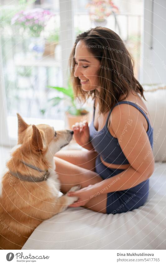 Millennial kaukasische Frau zu Hause mit Corgi Hund. Hundetrainer. Lustige gemütliches Bild der Frau mit Welpe in der Wohnung. Brunette lächelnd mit welsh Corgi Pembroke Hund sitzt auf Couch.