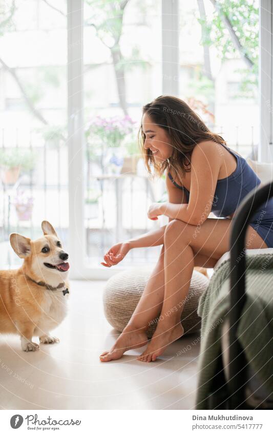 Millennial kaukasische Frau zu Hause mit Corgi Hund. Lustige gemütliche Bild der Frau mit Welpen in der Wohnung. Brunette lächelnd mit welsh Corgi Pembroke Hund sitzt auf Couch.