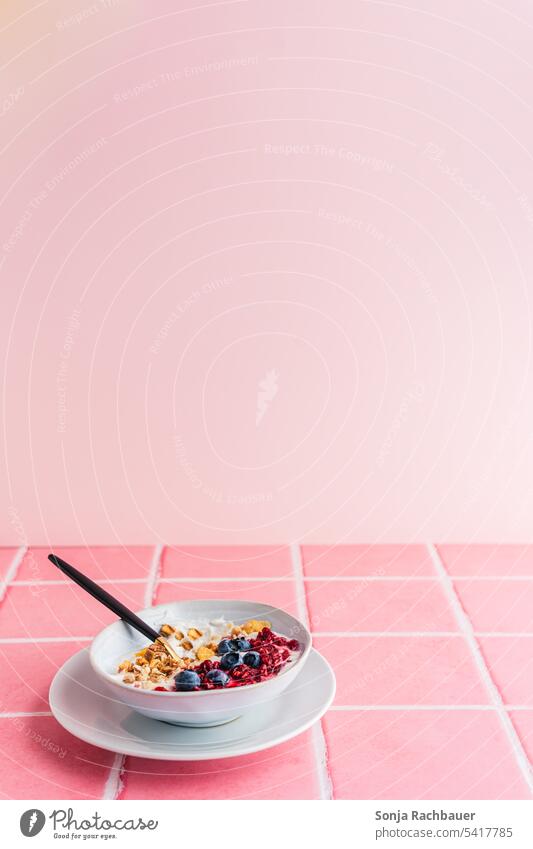 Eine Schüssel mit Joghurt, Müsli und frischen Beeren auf rosa Kacheln. Gesundes Frühstück. Gesundheit Lebensmittel süß Morgen modern minimalistisch farbenfroh