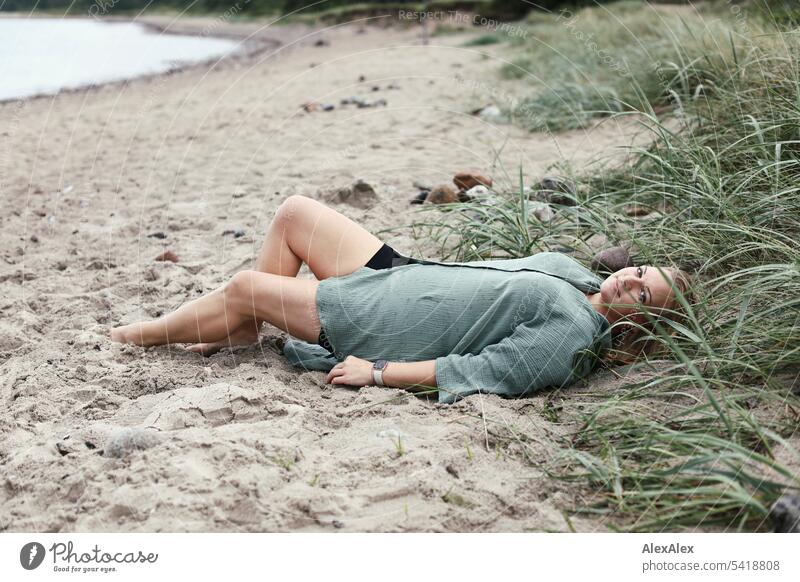 Portrait einer schönen, blonden Frau die im Sand am Strand liegt langhaarig blonde Haare Freude Lächeln Dünengras Schönheit entspannt relaxed natürlich draussen
