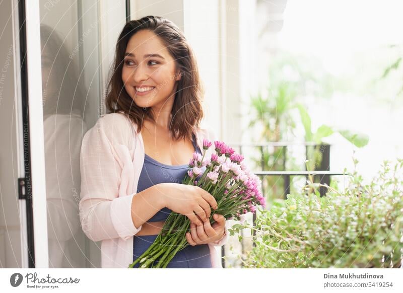 Schöne Frau mit Blumenstrauß auf dem Balkon. Glückliche Brünette lächelnd. Pflanzen und Blumen Gartenarbeit Hobby. Balkonpflanze Balkondekoration Sommer