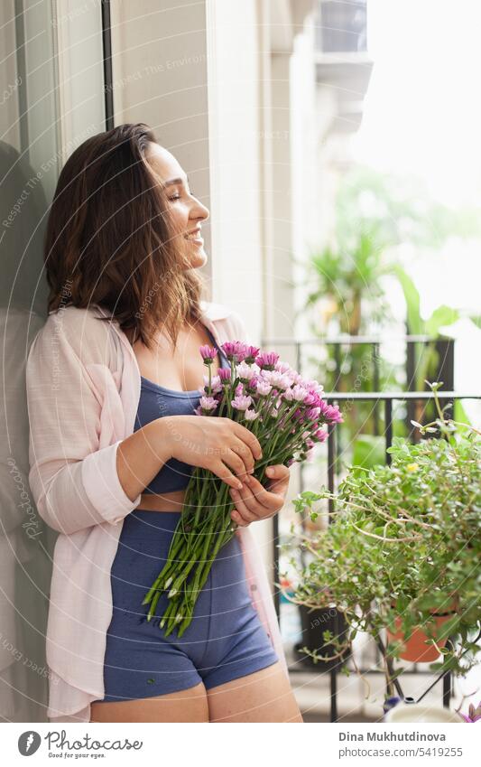 Schöne Frau mit Blumenstrauß auf dem Balkon Großaufnahme. Glückliche Brünette lächelnd. Pflanzen und Blumen Gartenarbeit Hobby. Balkonpflanze Balkondekoration