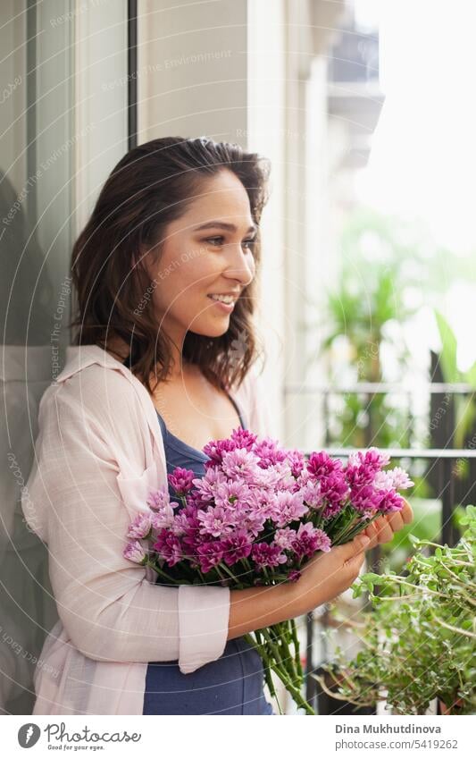 Schöne Frau mit Blumenstrauß auf dem Balkon. Glückliche Brünette lächelnd. Pflanzen und Blumen Gartenarbeit Hobby. Balkonpflanze Balkondekoration Sommer