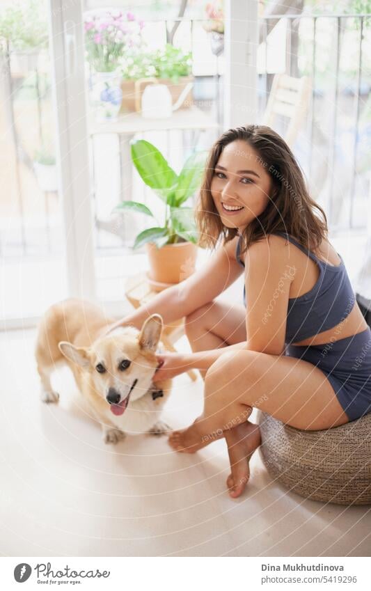 Millennial kaukasische Frau zu Hause mit Corgi Hund. Lustige gemütliche Bild der Frau mit Welpen in der Wohnung. Brunette lächelnd mit welsh Corgi Pembroke Hund sitzt auf Couch.