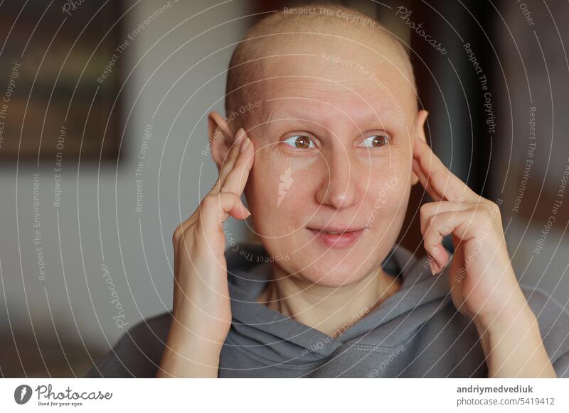 Glatzköpfige Frau, die mit den Fingern den Kopf berührt, leidet unter Kopfschmerzen nach einer Chemotherapie. Unglückliche haarlose krebskranke Frau mit Migräne zu Hause. Onkologie-Konzept. Gesundheitswesen, Medizin