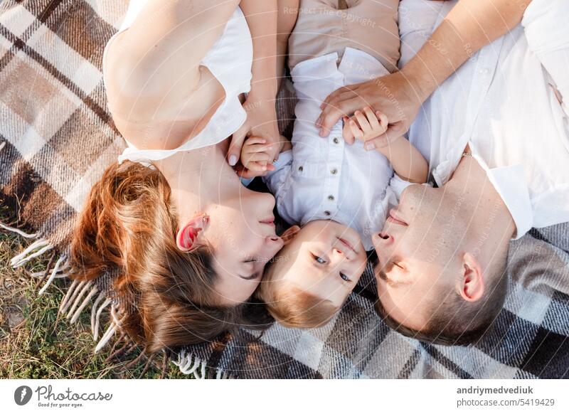 Mama, Papa und der kleine Sohn liegen auf einer Decke im Sommerpark. Das Konzept des Sommerurlaubs. Muttertag, Vatertag, Babytag. Familie verbringt Zeit zusammen in der Natur. Familie Blick