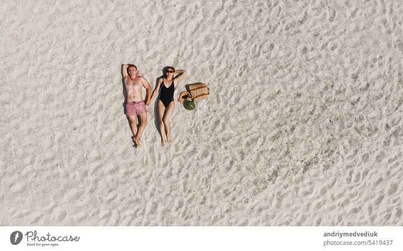 Luftaufnahme eines jungen Paares, das am weißen Sandstrand liegt. Mann und Frau in Badekleidung verbringen Zeit miteinander und reisen durch die Wüste Lügen