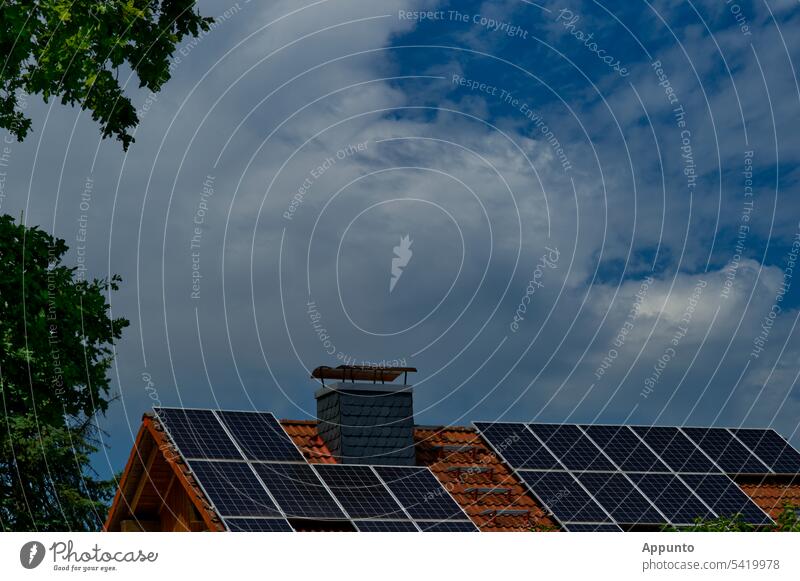 Solarmodule auf einem Hausdach mit roten Dachpfannen und schieferverkleidetem Kamin Solarzellen Solardach Baumwipfel Himmel blau wolkig Wolken Energie Strom