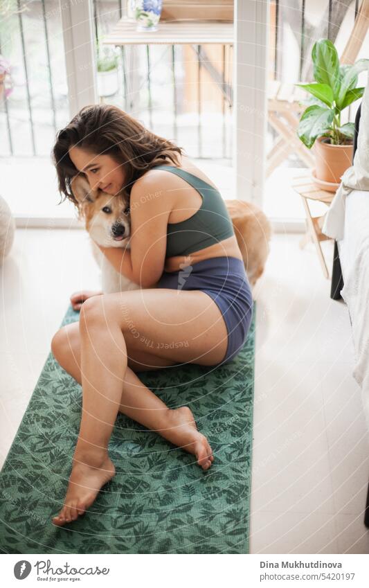 Junge Frau mit Corgi Pembroke Hund macht Yoga auf grüner Matte zu Hause. Praktiziert Sport, Wellness und Gesundheit. Indoor Yoga Online-Kurs. Achtsamkeit und Meditation, aktiver Lebensstil.