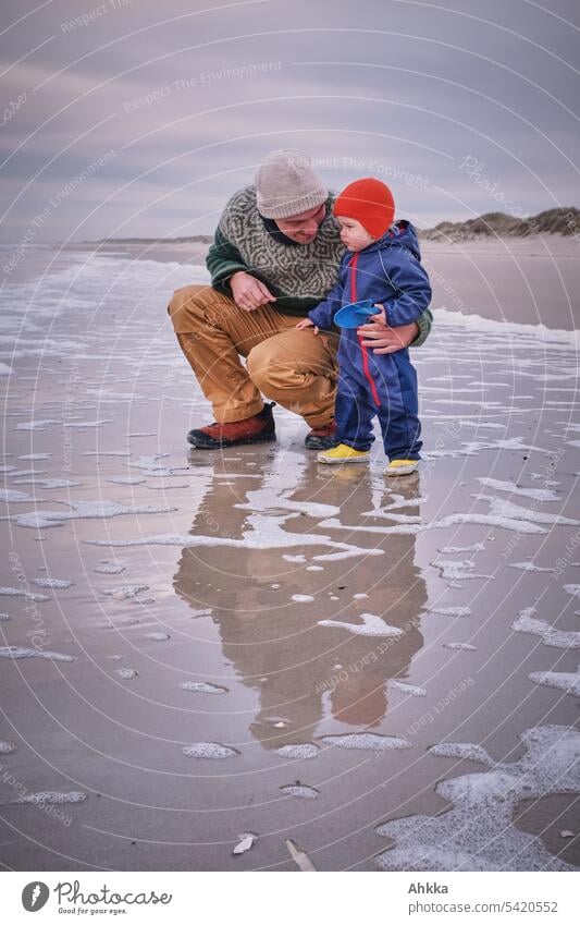 Mann mit Kleinkind warm angezogen am menschenleeren Strand Vater Meer Zuneigung Wasser Wellen Küste Zusammensein begleiten im Freien natürlich Urlaub neugierig