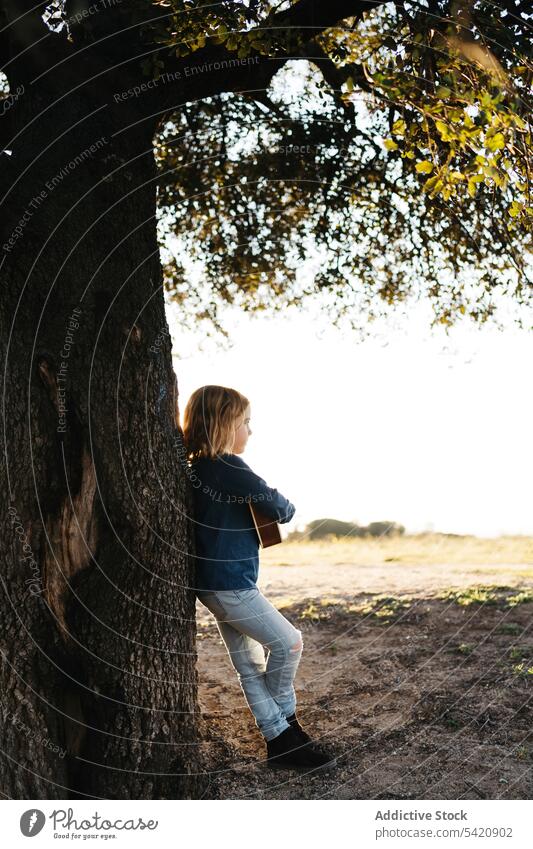 Kleines Mädchen steht unter einem Baum und spielt Ukulele Kind spielen Musik Gitarre Stehen Natur Sommer ernst wenig Instrument Klang Gesang Melodie Kofferraum