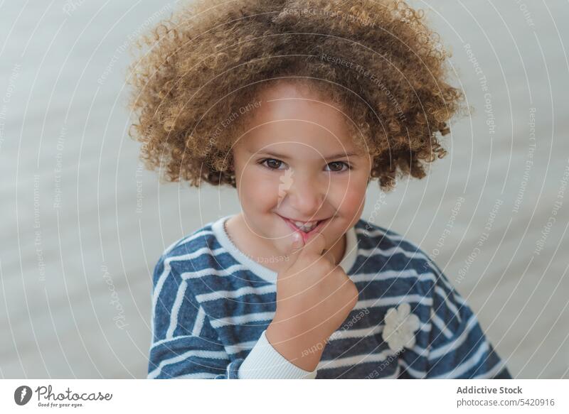 Glückliches ethnisches kleines Mädchen auf der Straße heiter niedlich Kind krause Haare bezaubernd Lächeln trendy lässig Freude Kindheit wenig positiv charmant
