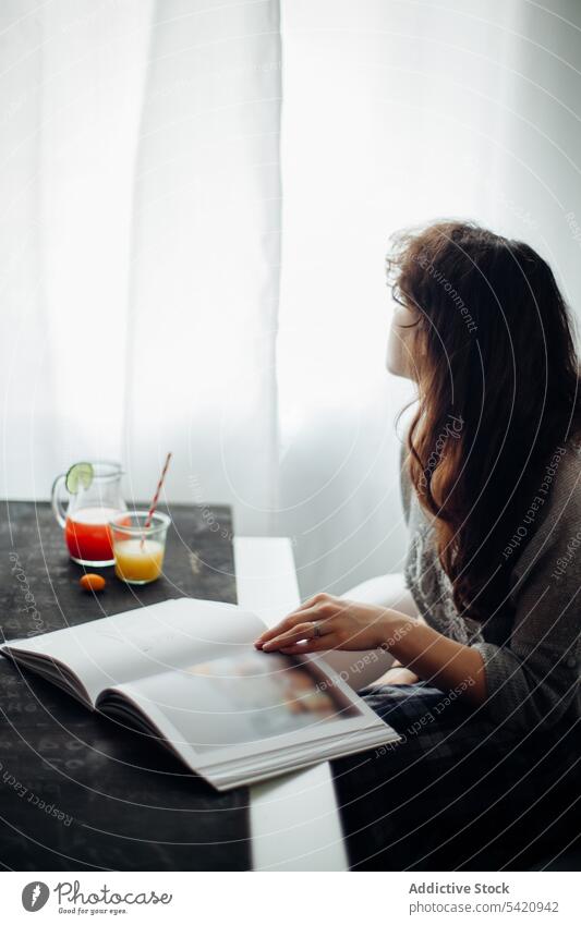 Junge Frau liest Buch am Tisch mit Saft lesen trinken ruhen heimwärts sich[Akk] entspannen besinnlich jung Lifestyle Literatur lässig Morgen Fenster Hobby
