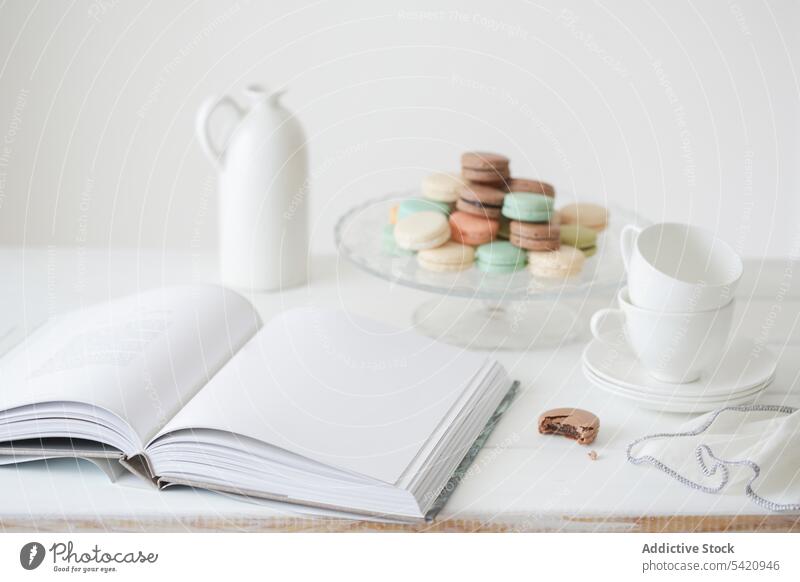 Makronen auf weißem Tisch mit Buch und Geschirr Tasse Dessert süß Kulisse Page Zusammensetzung Tee geschmackvoll Lebensmittel lecker farbenfroh sanft Design