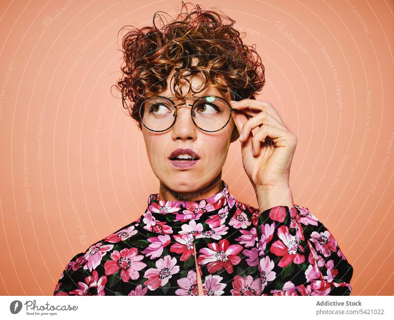 Zweifelnde Frau in trendigem Outfit Mode Stil nachdenklich trendy Brille farbenfroh geblümt jung Model besinnlich Stoff Accessoire krause Haare altehrwürdig
