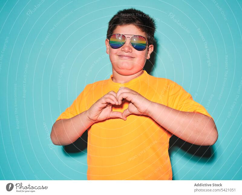 Glücklicher Junge zeigt Herzzeichen mit Händen Kind gestikulieren Stil Sonnenbrille Lächeln positiv mollig lässig hell gelb Farbe männlich heiter trendy zeigen